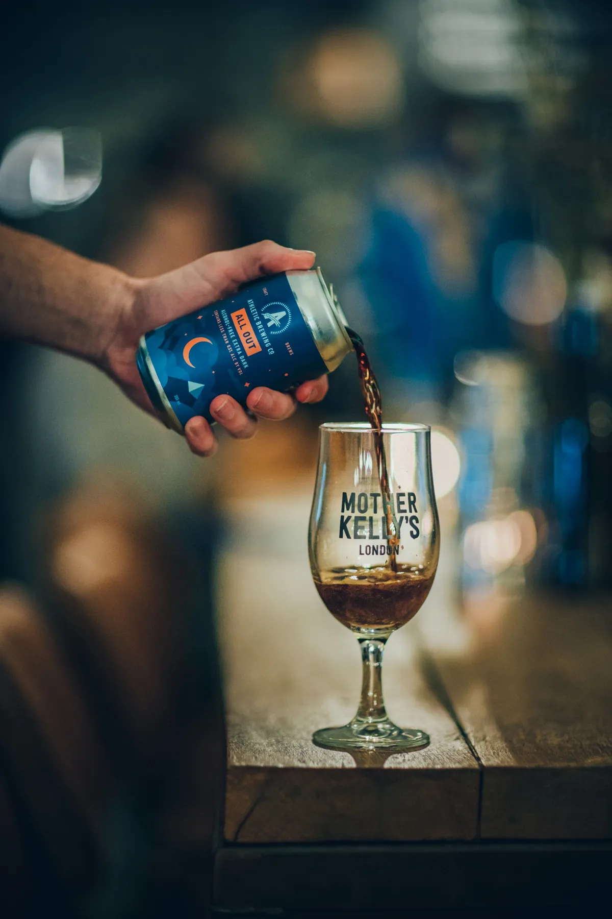 Hand pouring a can of dark beer into a stemmed glass on a pub table, Athletic Brewing Company