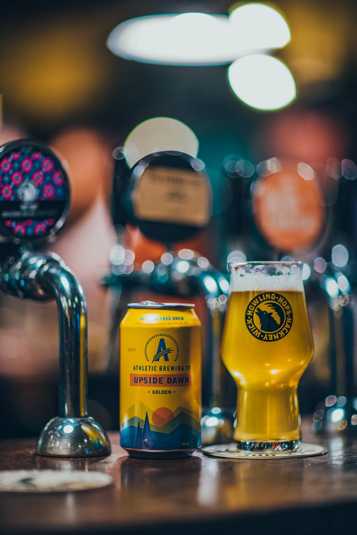 Upside Dawn can and a full pint on a bar in front of the beer taps, Athletic Brewing Company
