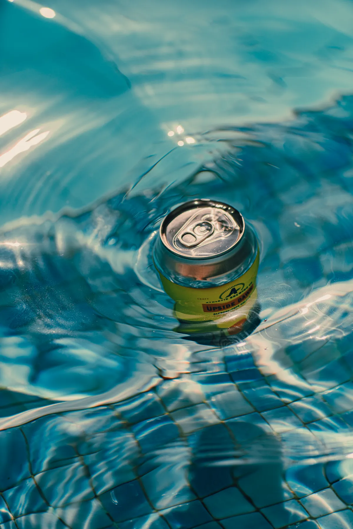 Can floating on rippling turquoise pool water, seen from above, Athletic Brewing Company shoot