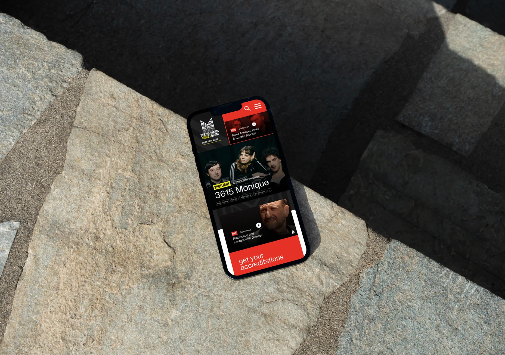 Phone lying on a stone slab in the sun, showing the Séries Mania Forum homepage on mobile