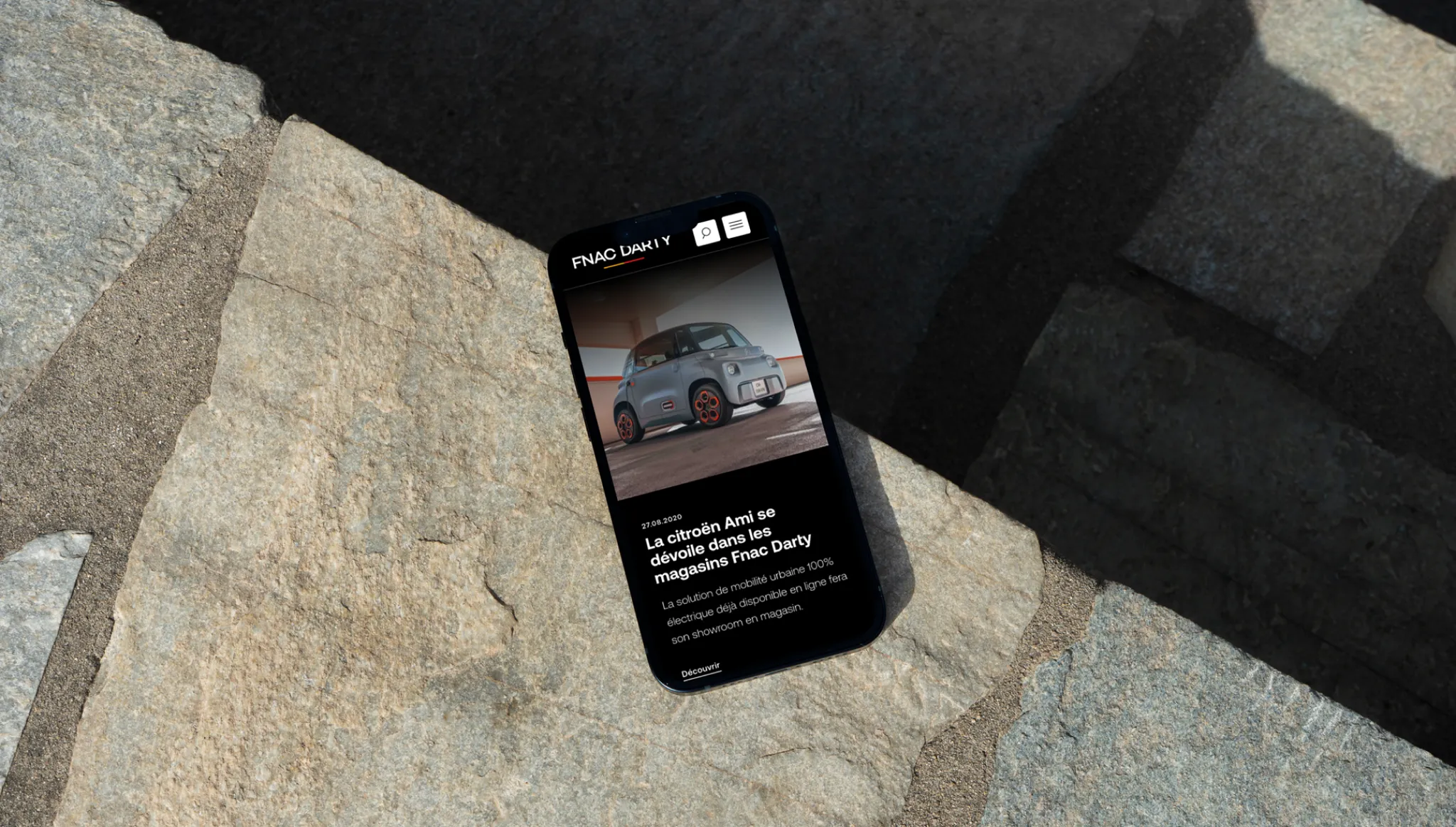 Phone lying on a stone slab in the sun, showing a news article from the Fnac Darty group website