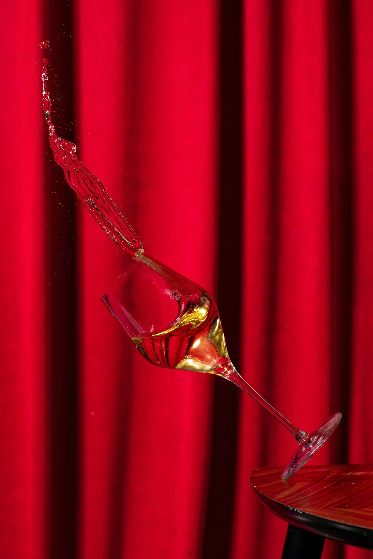 Champagne splashing out of a tilting glass against a red velvet curtain, Nicolas Feuillatte