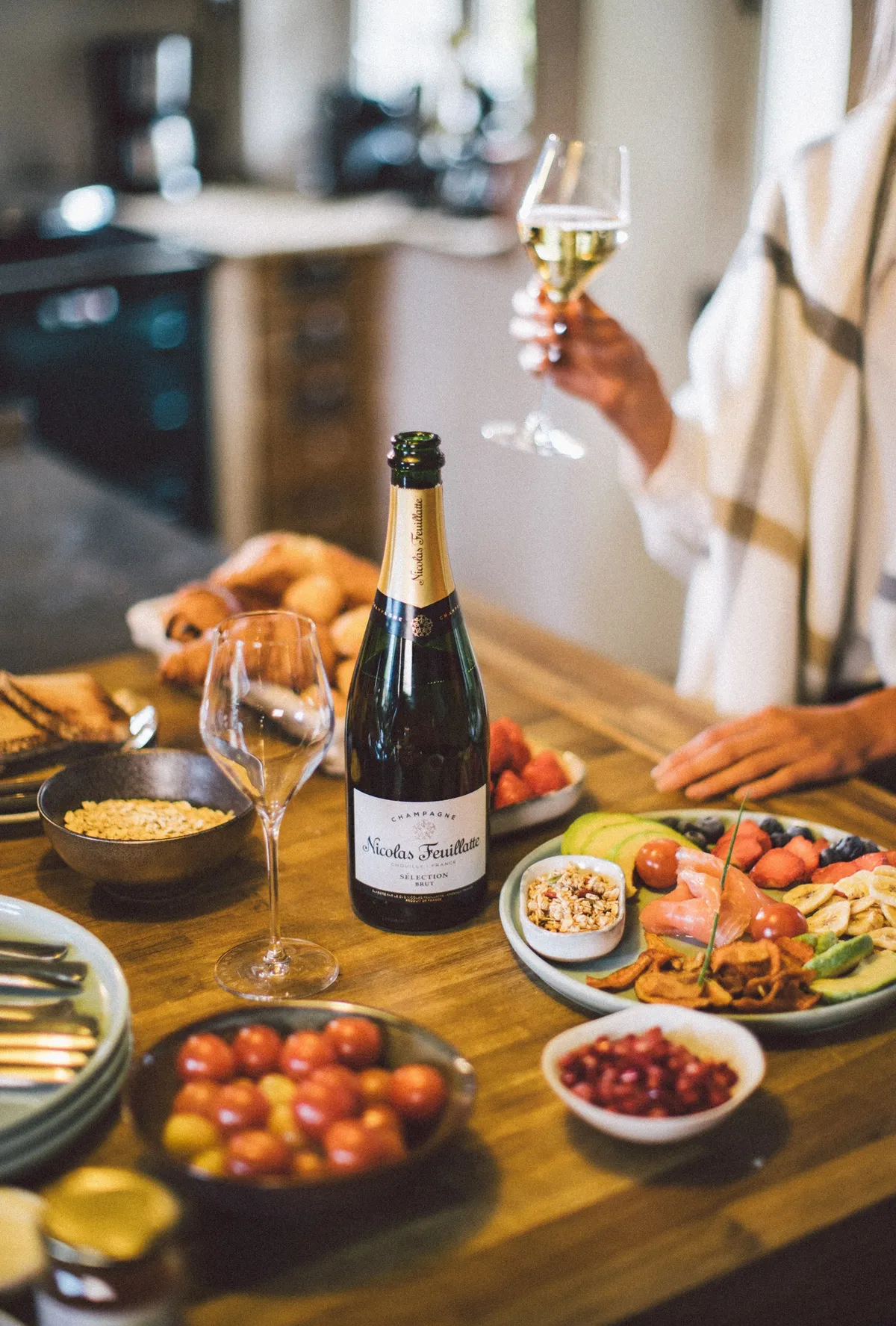Festive table with a bottle of Nicolas Feuillatte, sharing plates and a hand raising a flute of champagne