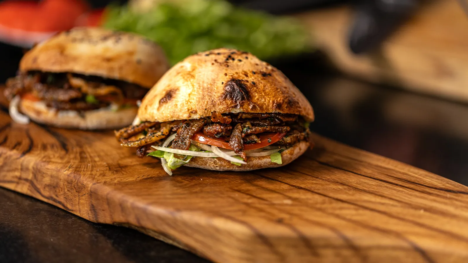 Two kebab buns filled with meat and salad on a wooden board, one of the sandwiches of Graille sur le rail