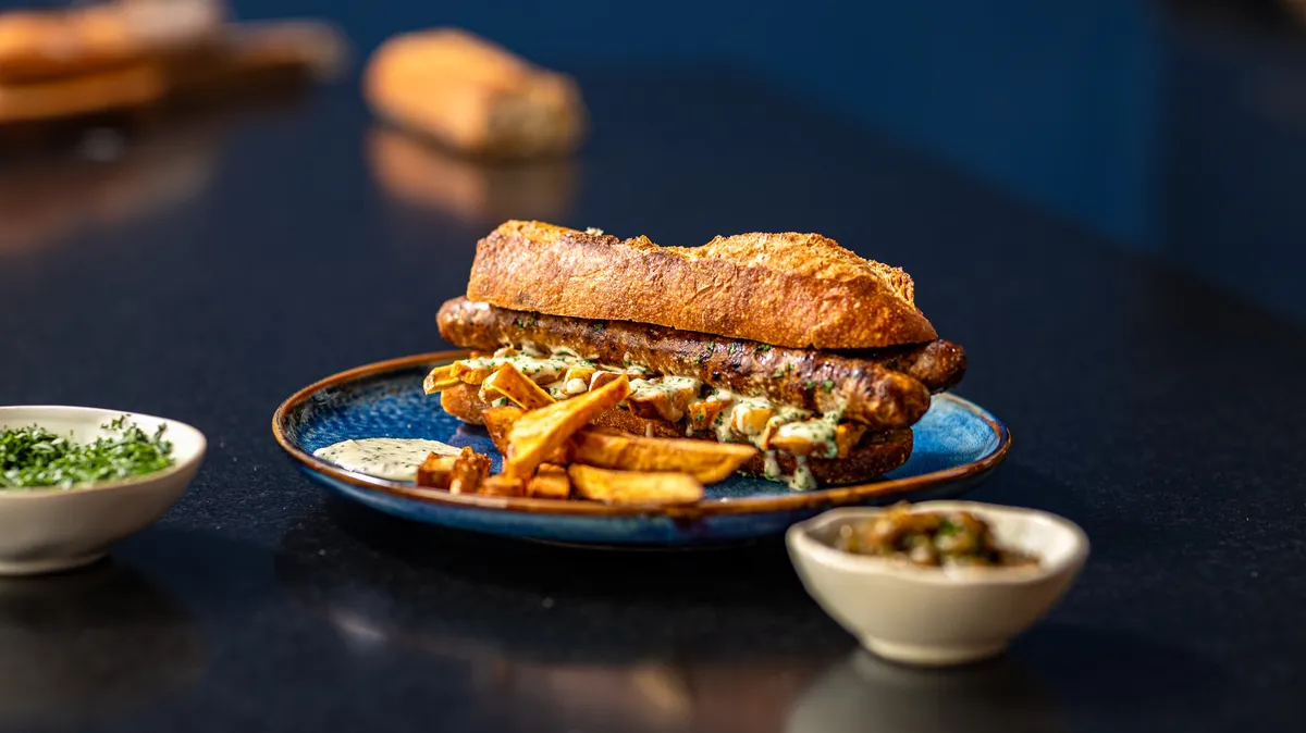 Merguez and fries baguette on a blue plate with herbs and sauces, one of the sandwiches of Graille sur le rail