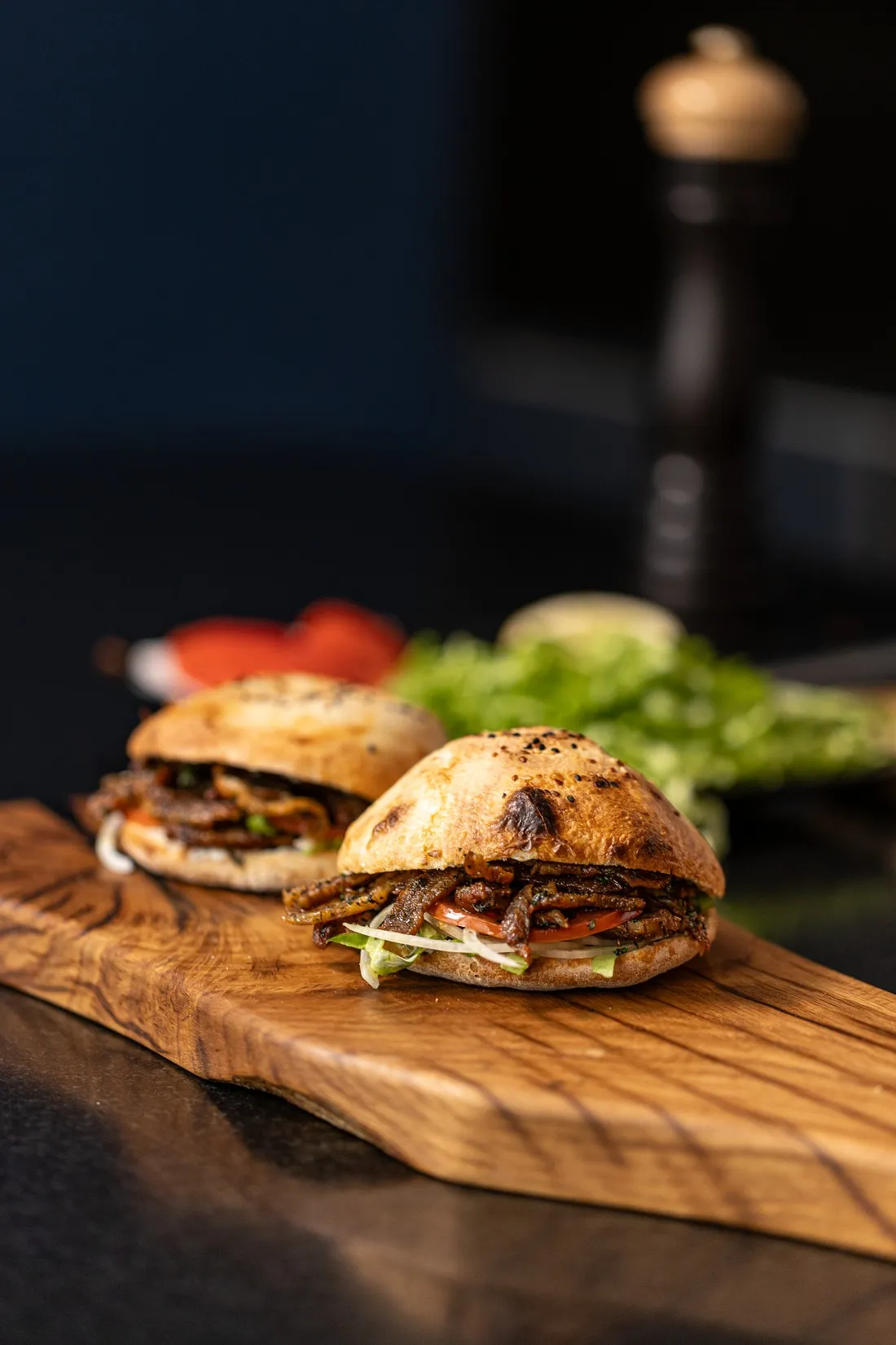 Kebab buns on a wooden board in low light, a pepper mill behind, food shot for Graille sur le rail