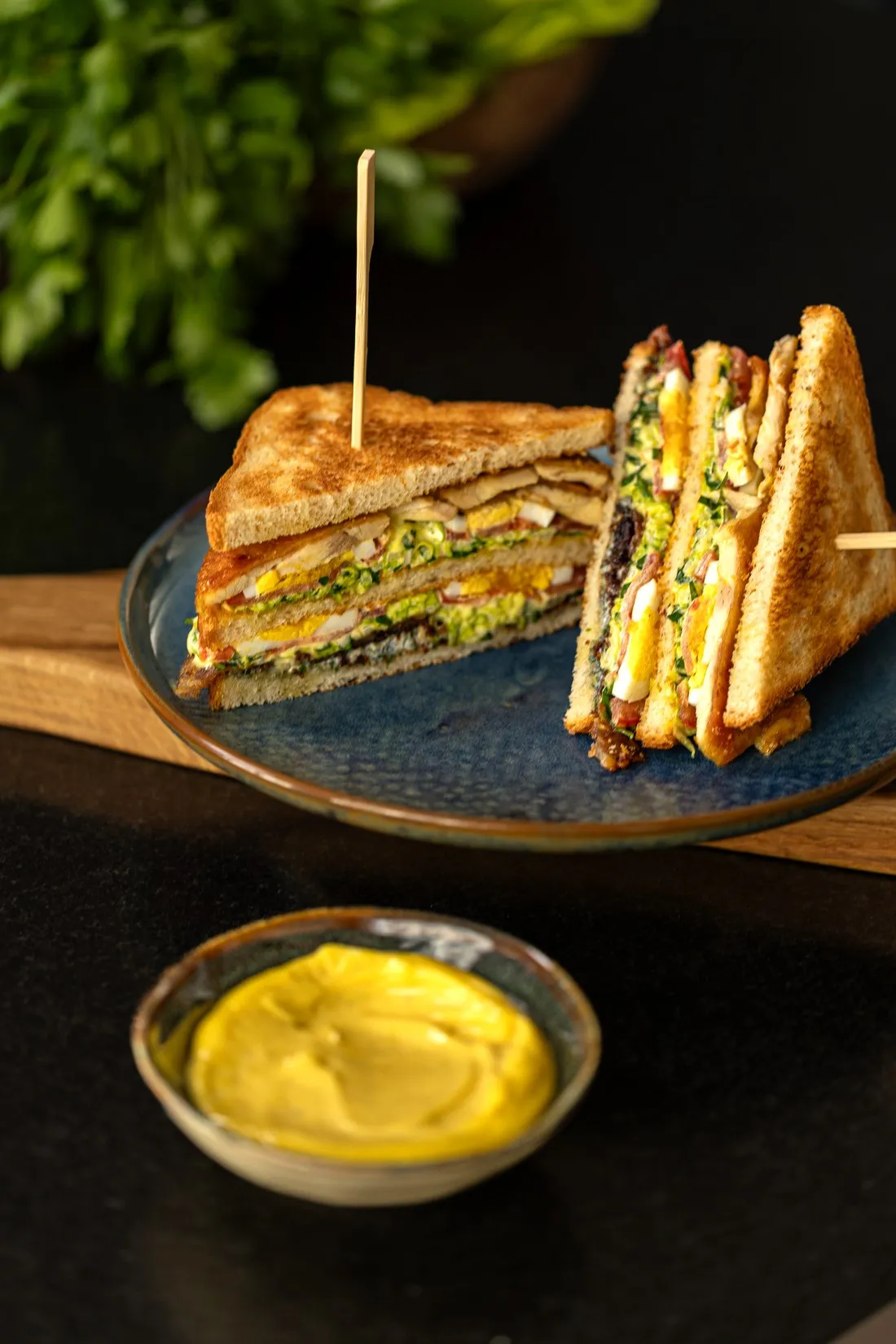 Toasted club sandwich on a blue plate with a bowl of mustard sauce, food shot for Graille sur le rail