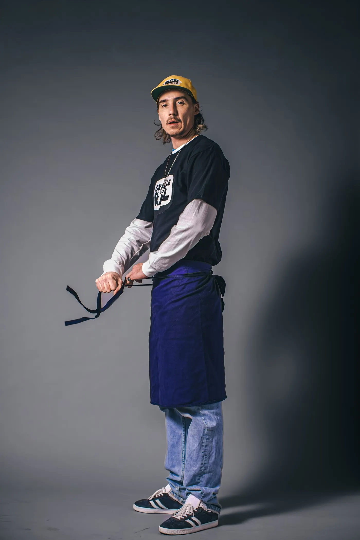 Scotchman standing in an apron and cap on a grey studio background, portrait for Graille sur le rail