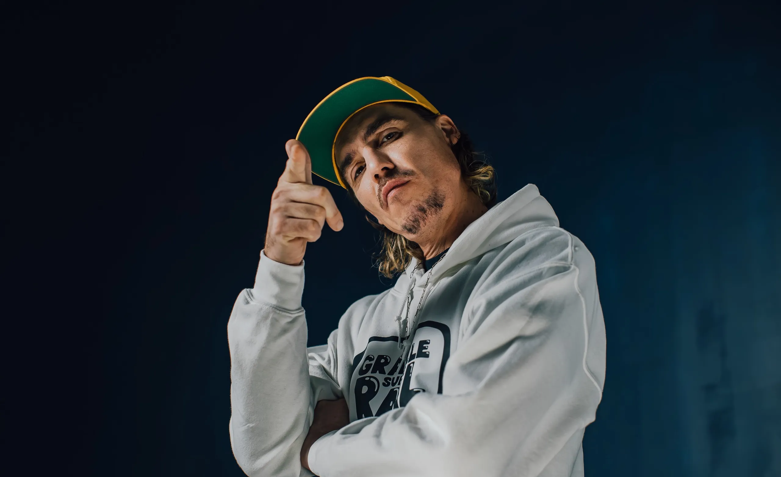 Scotchman pointing at his cap in the Graille sur le rail hoodie against a dark background, France 3 show