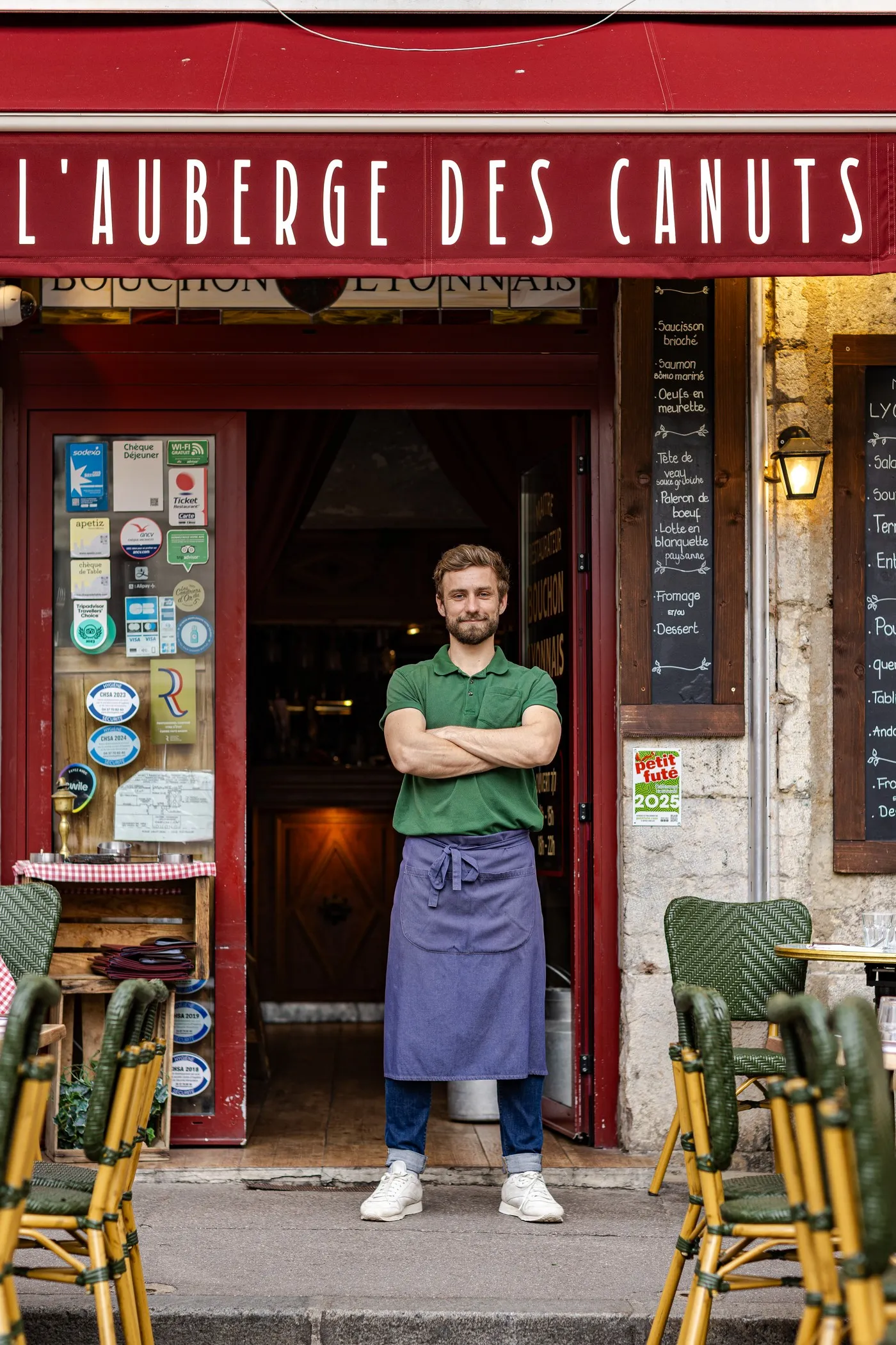 Waiter in an apron, arms crossed, at the door of L'Auberge des Canuts, a bar serving La Canute Lyonnaise