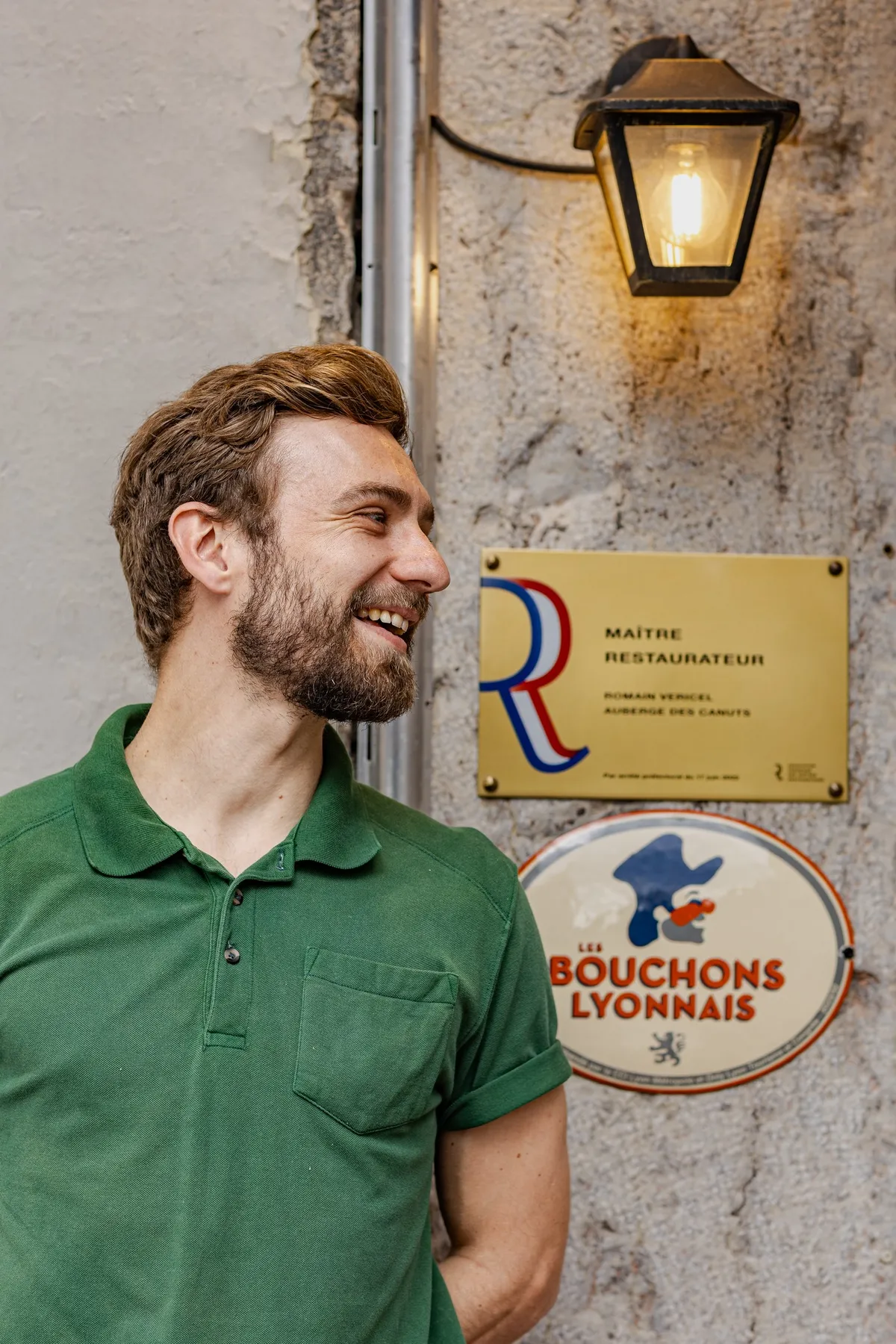Laughing man in a green polo beside a Bouchons Lyonnais plaque, a restaurant serving La Canute Lyonnaise