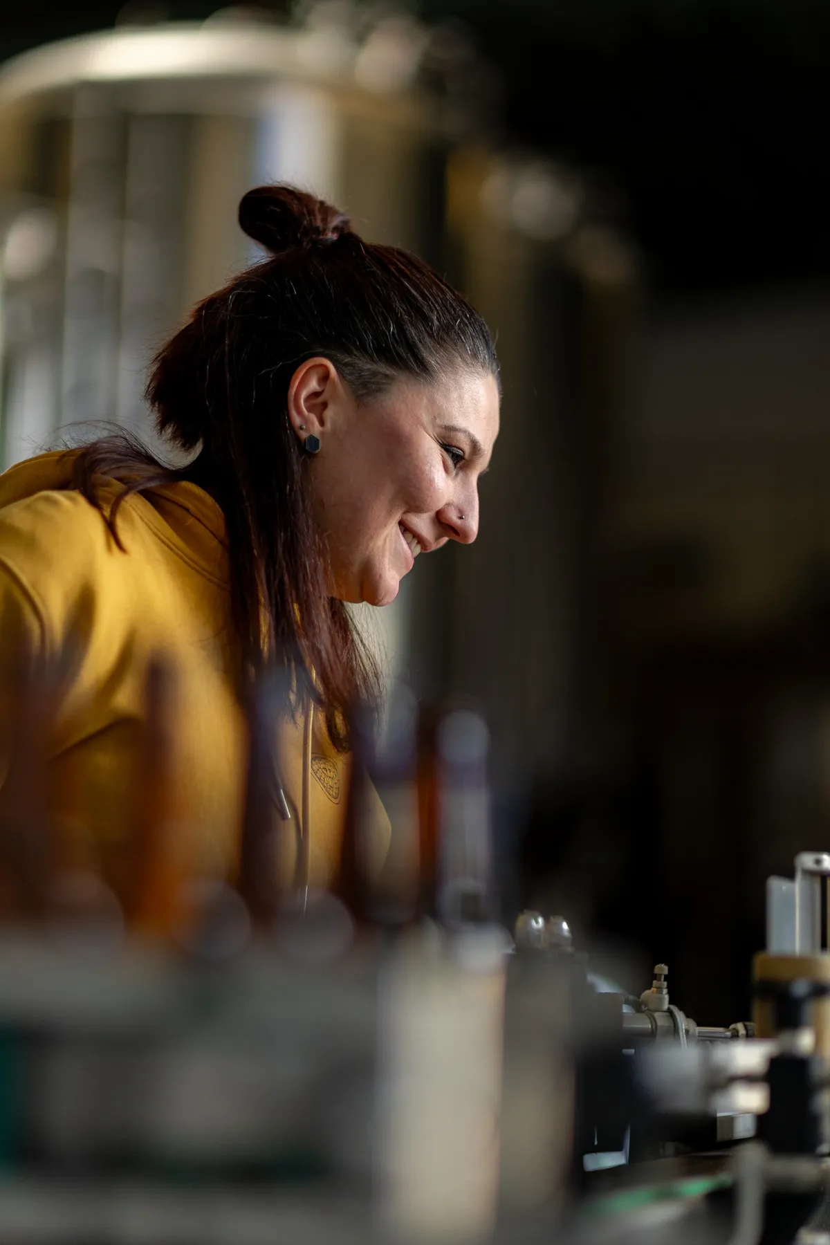 Smiling brewer with her hair in a bun leaning over the brewing equipment, La Canute Lyonnaise