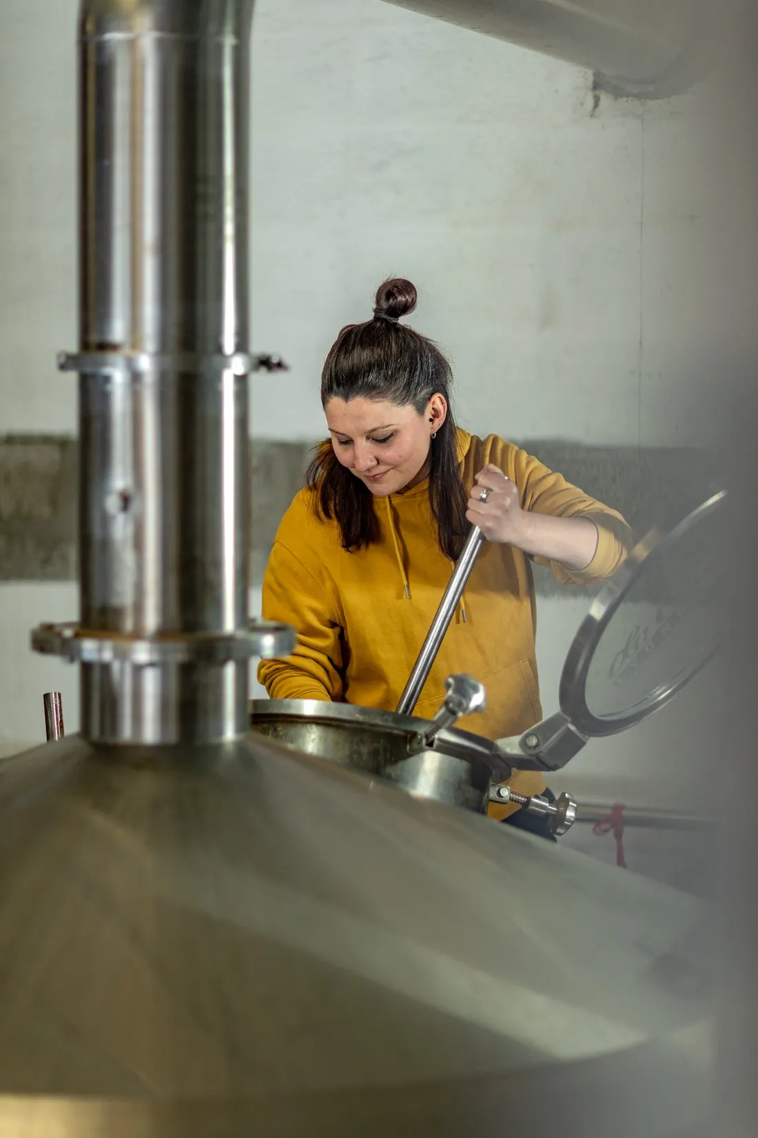 Brewer in a yellow hoodie stirring the mash in a steel tank, La Canute Lyonnaise brewery in Lyon