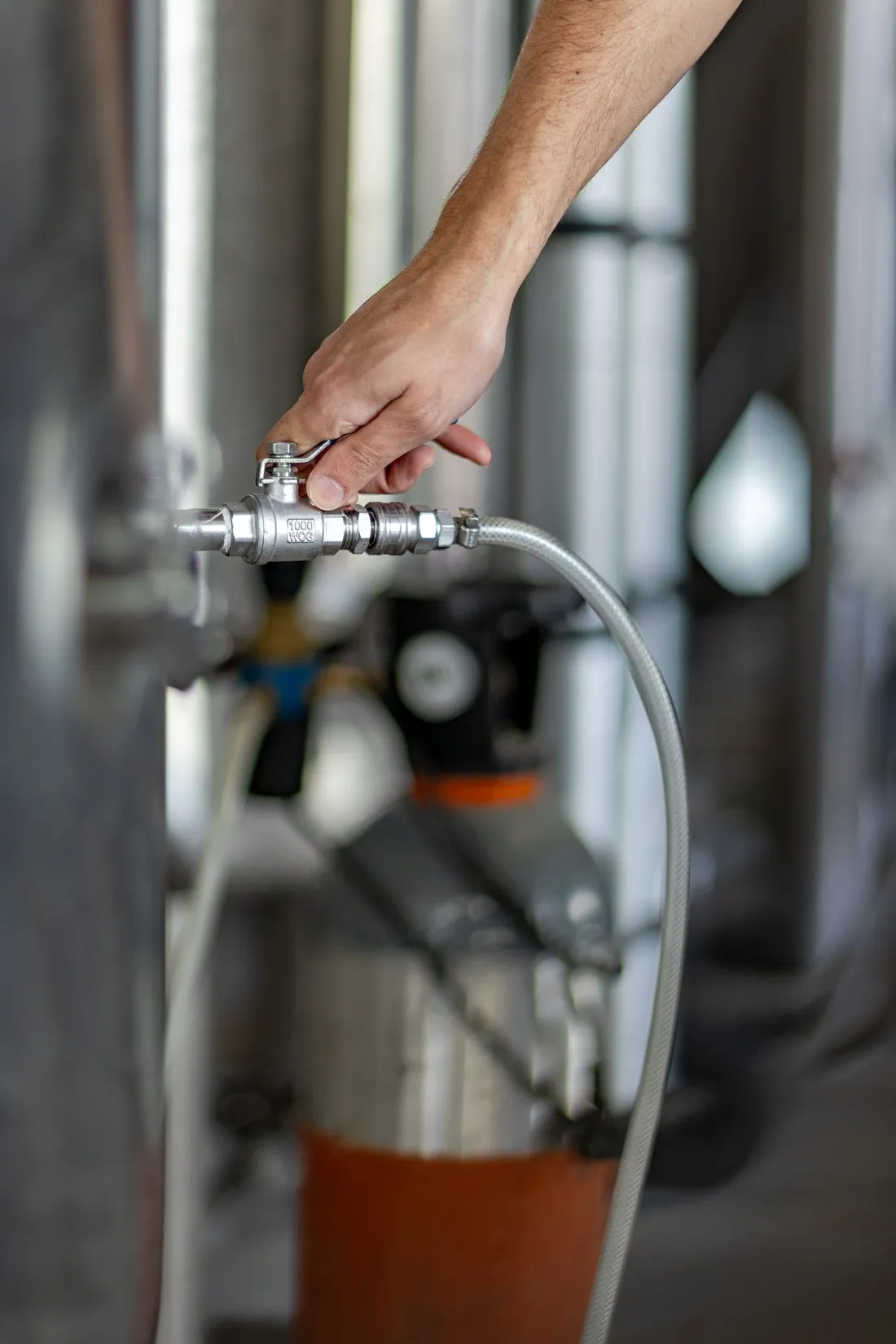 Hand opening a valve on a stainless steel brewing tank, La Canute Lyonnaise brewery in Lyon