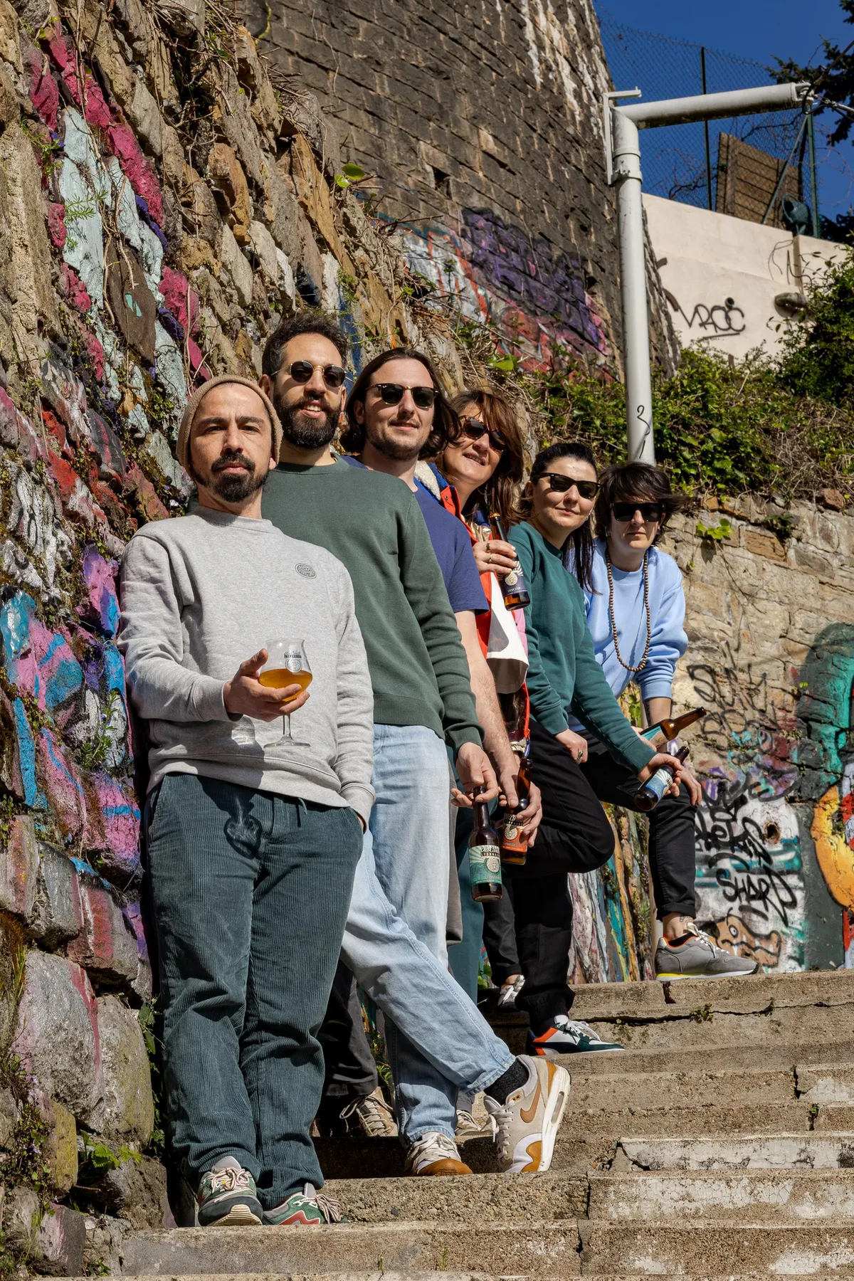 The team standing on steps along a graffiti-covered wall, one holding a glass, La Canute Lyonnaise