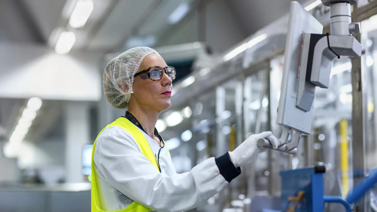 Operator in a hairnet and hi-vis vest checking a screen on the production line, L'Oréal factory, Le Monde