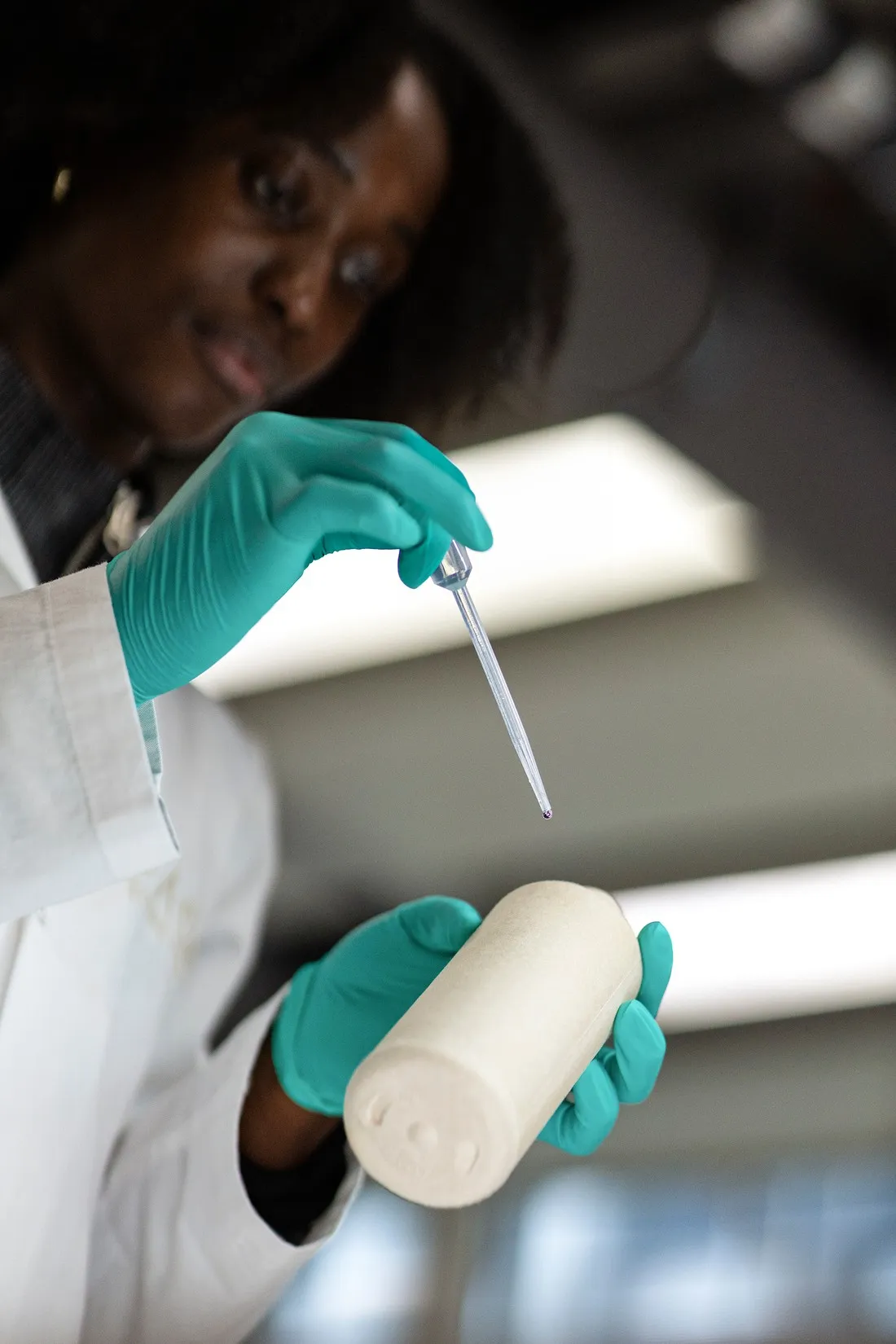 Researcher in green gloves using a pipette over a white container in the laboratory, Le Monde & L'Oréal