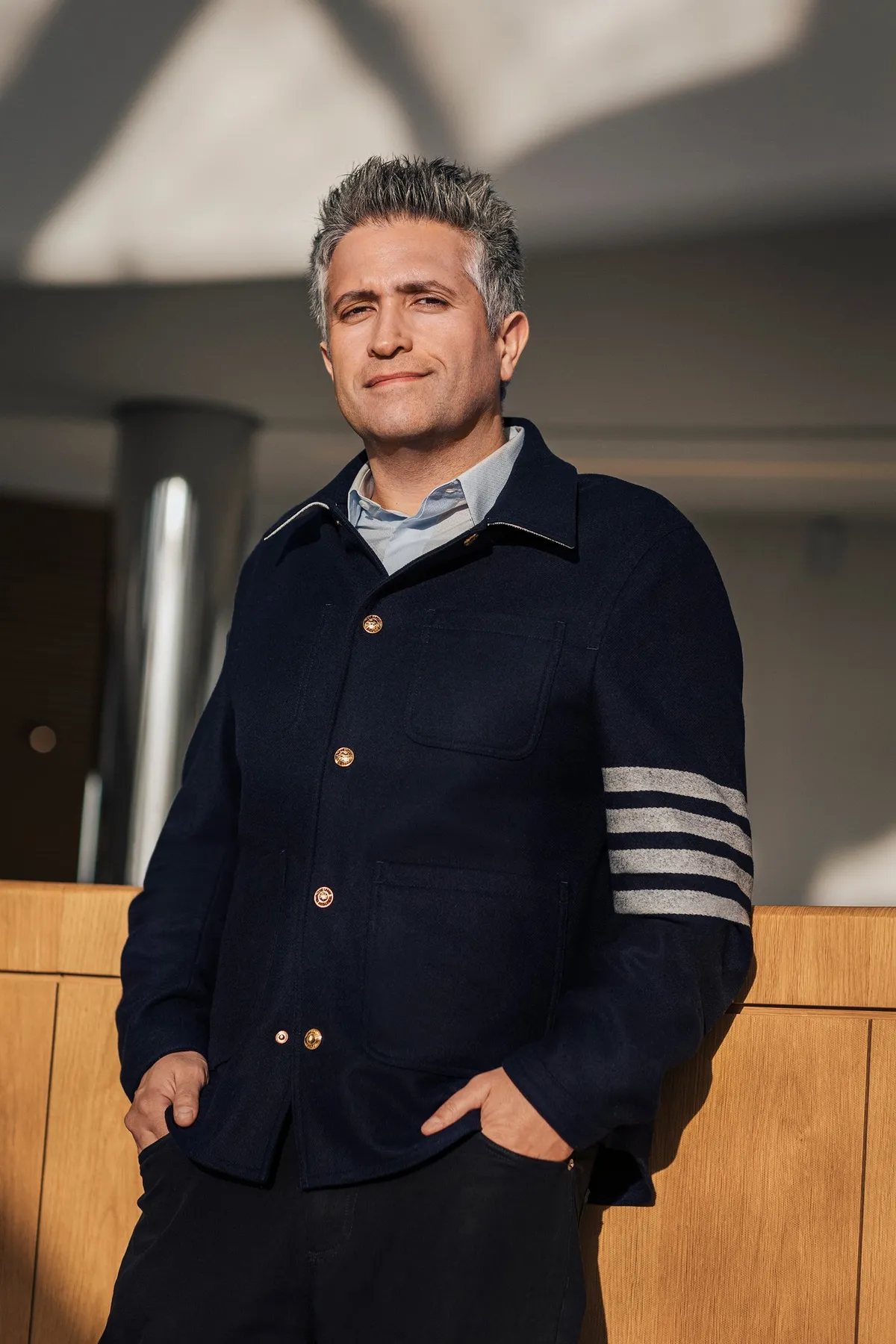 Grey-haired man in a navy jacket with striped sleeves, hands in pockets, portrait for Le Monde & L'Oréal