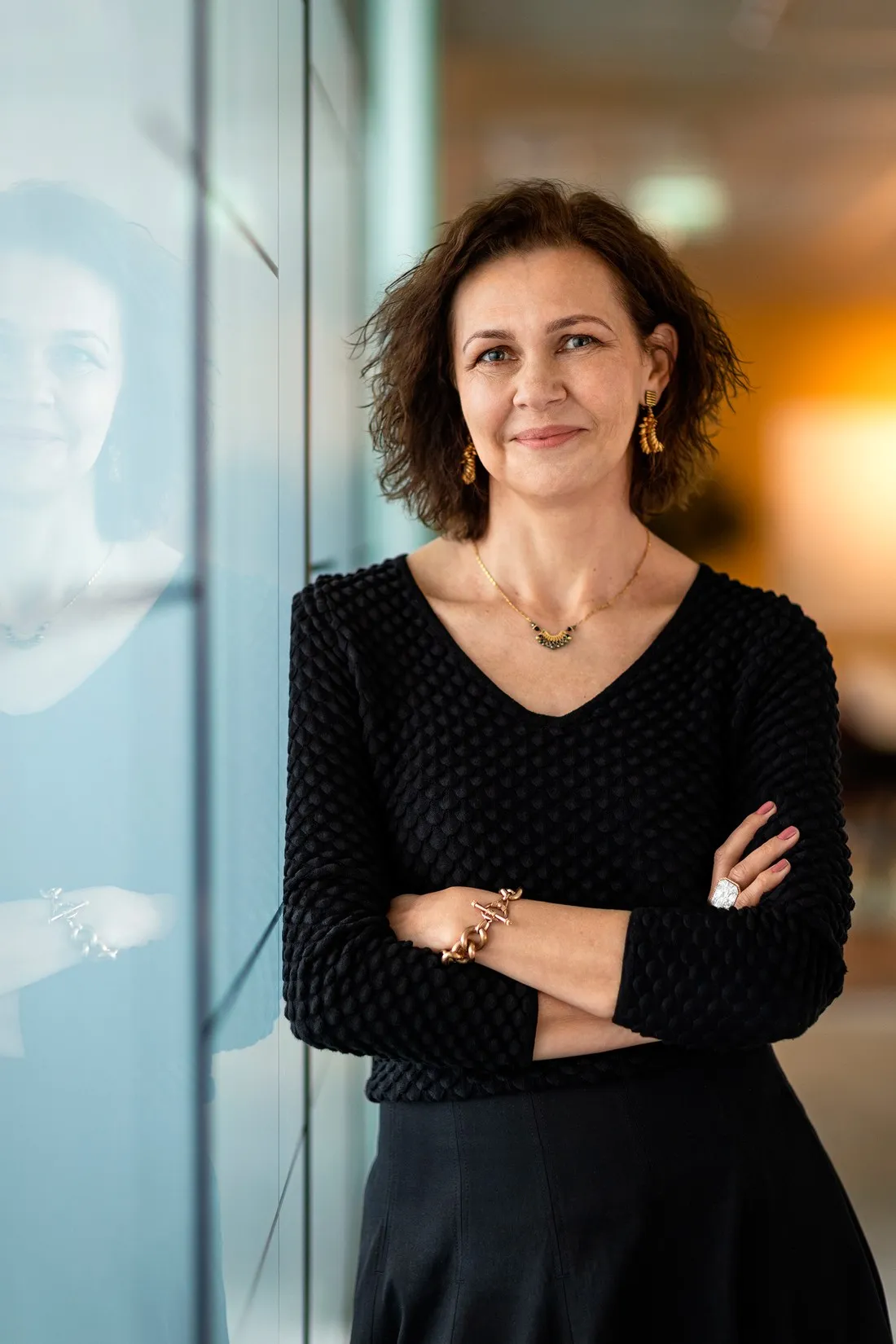 Woman in a black knit top, arms crossed, against a glass wall, portrait for Le Monde & L'Oréal