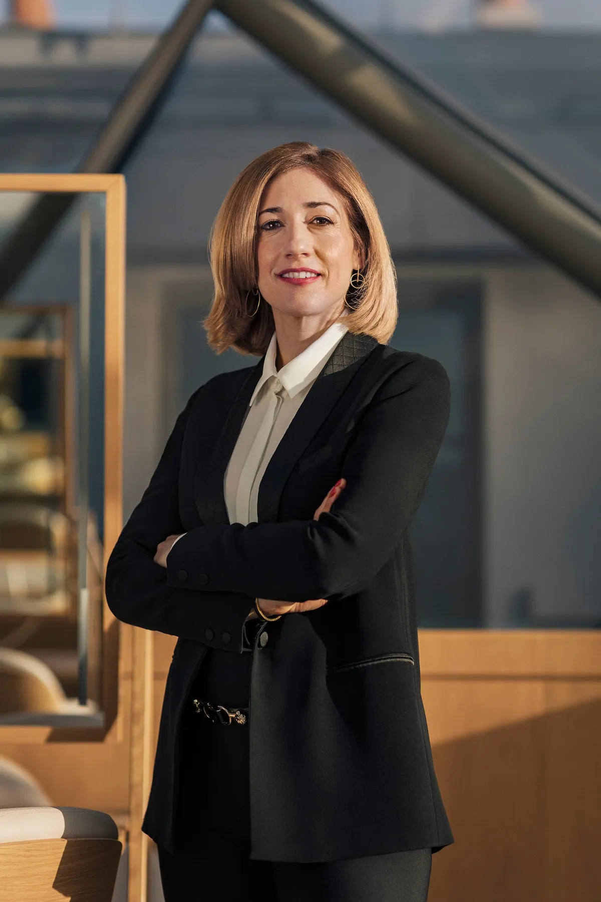 Woman in a black suit, arms crossed, beneath a steel structure, portrait for Le Monde & L'Oréal
