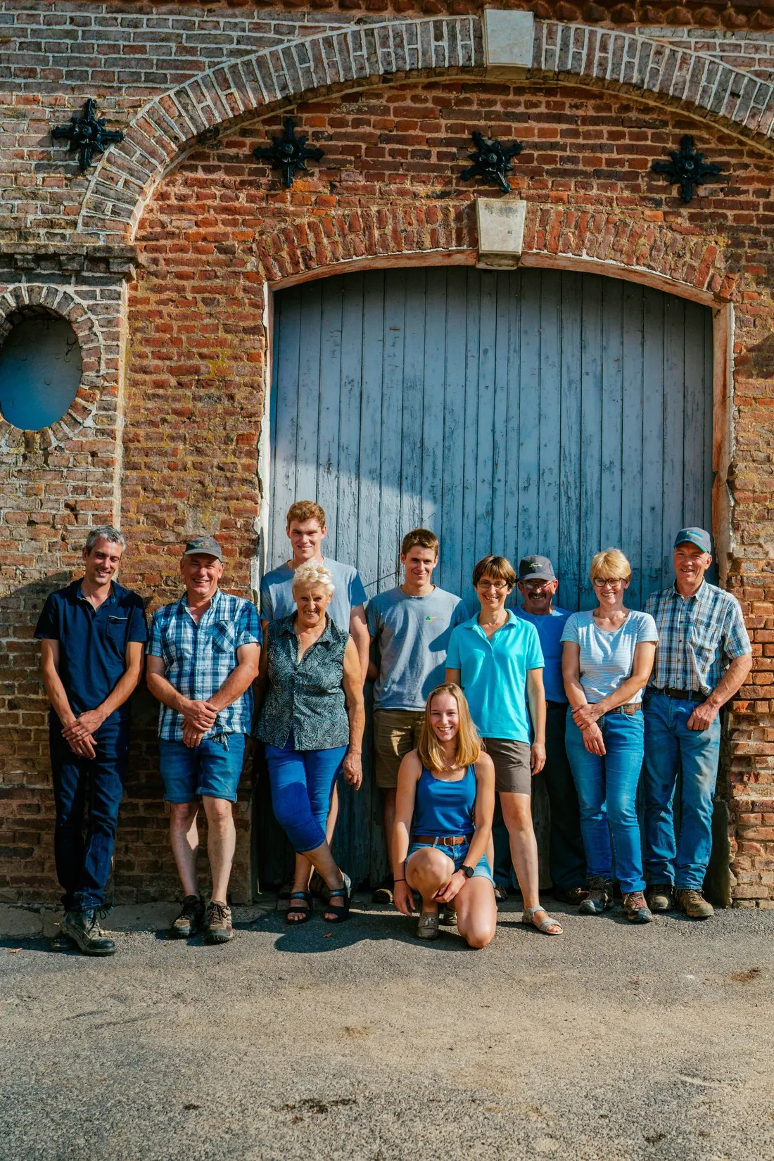 Farming family lined up in front of a brick barn with a blue wooden door, McCain farming families