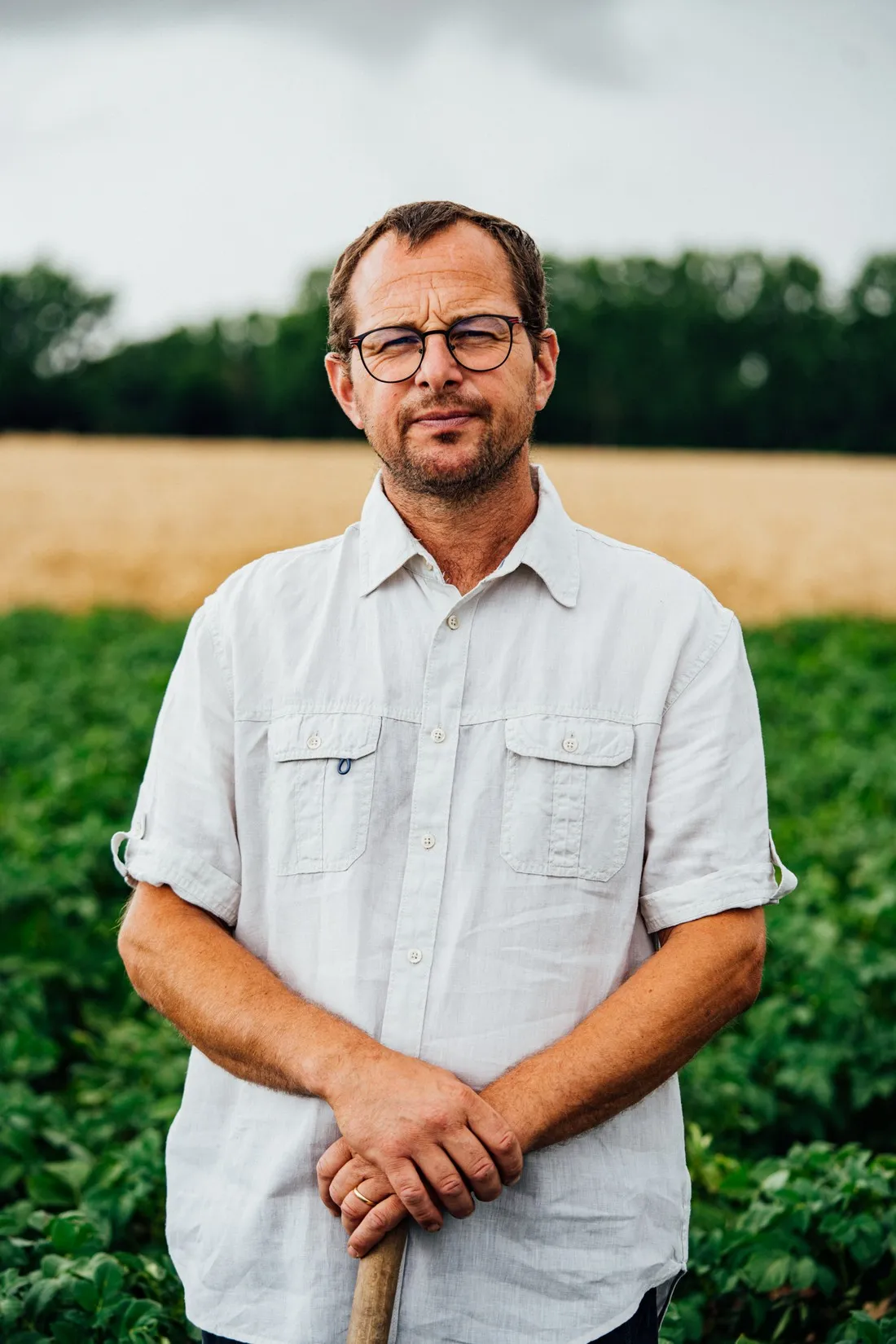 Farmer with glasses in a white shirt leaning on a tool in a potato field, McCain regenerative agriculture