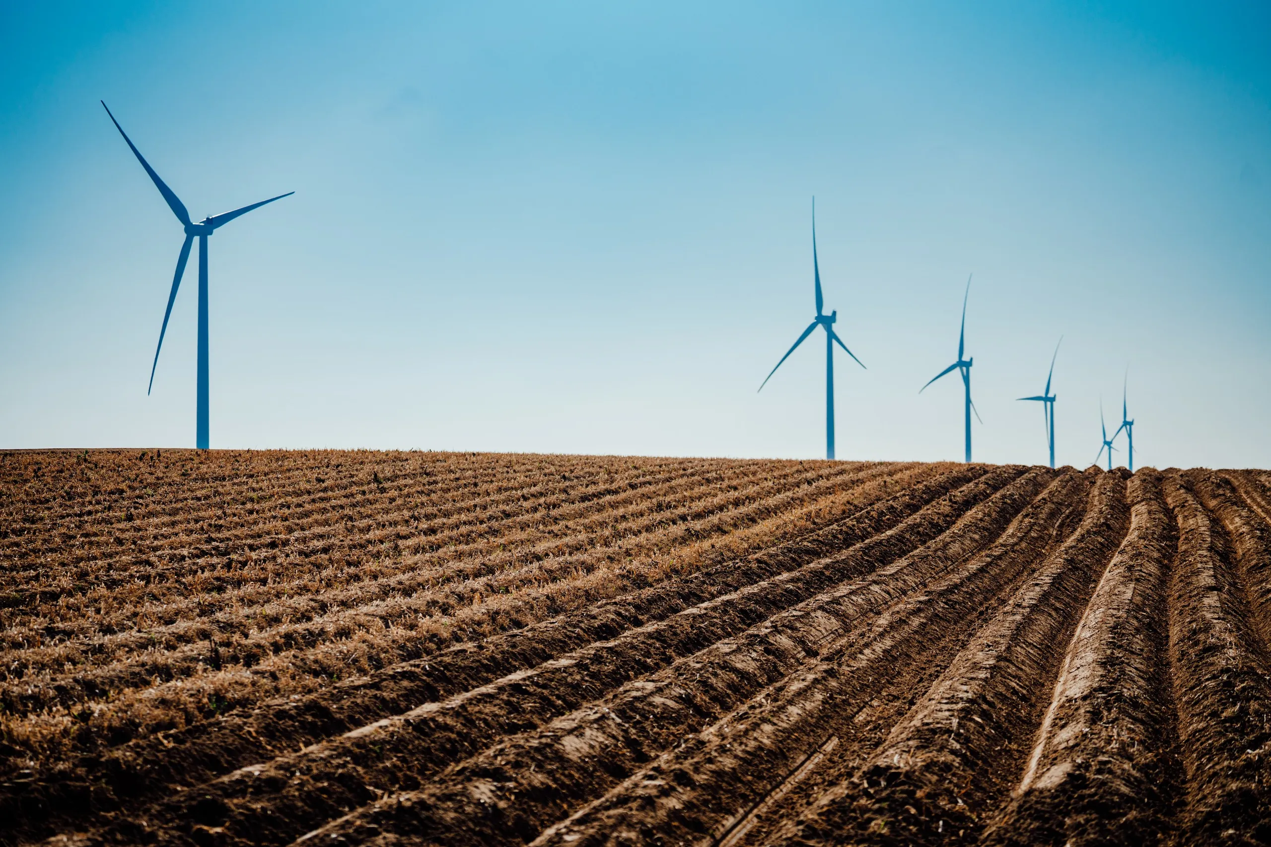 Wind turbines standing over a freshly ploughed field under a clear sky, McCain regenerative agriculture