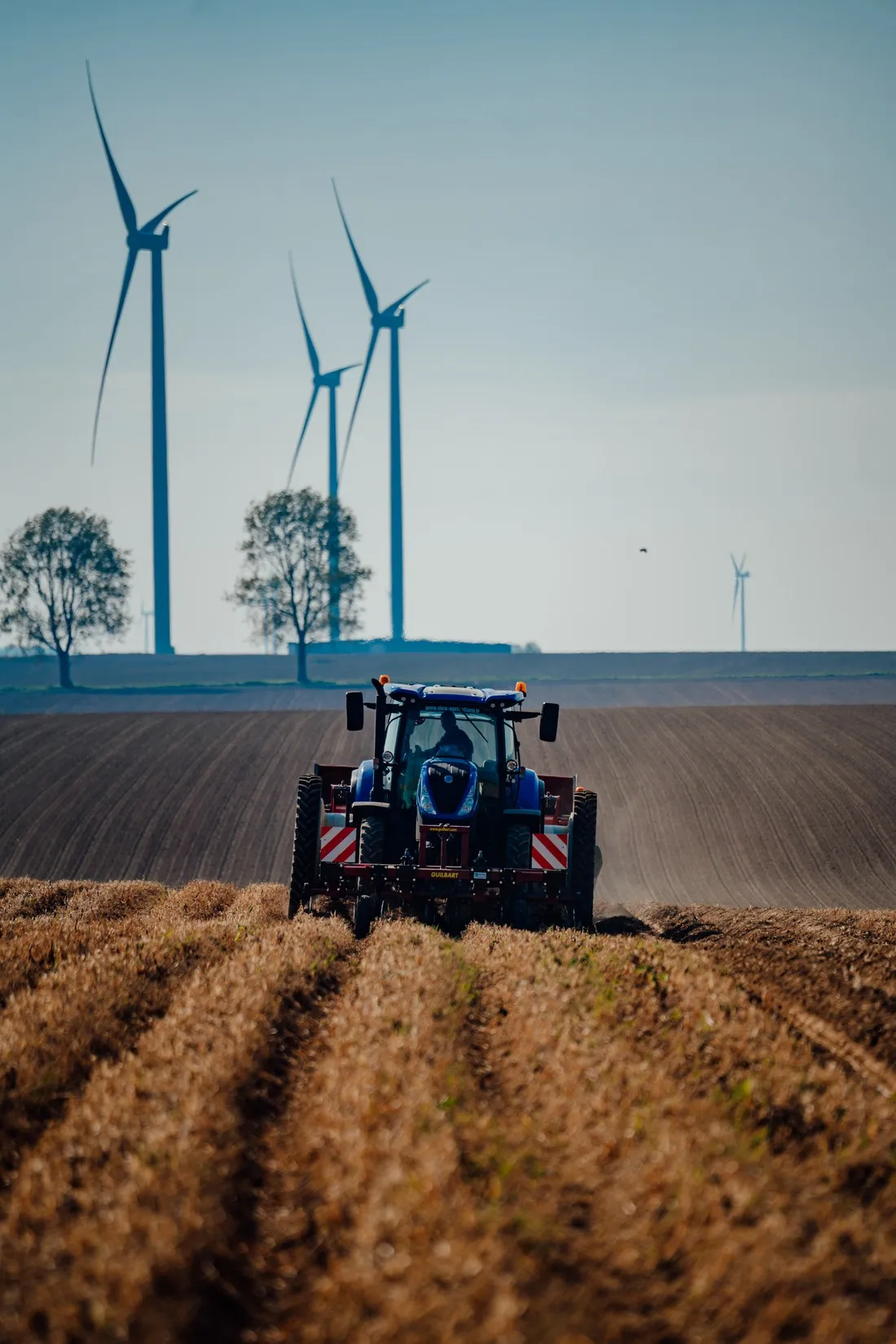 Blue tractor working a field below three wind turbines, McCain regenerative agriculture