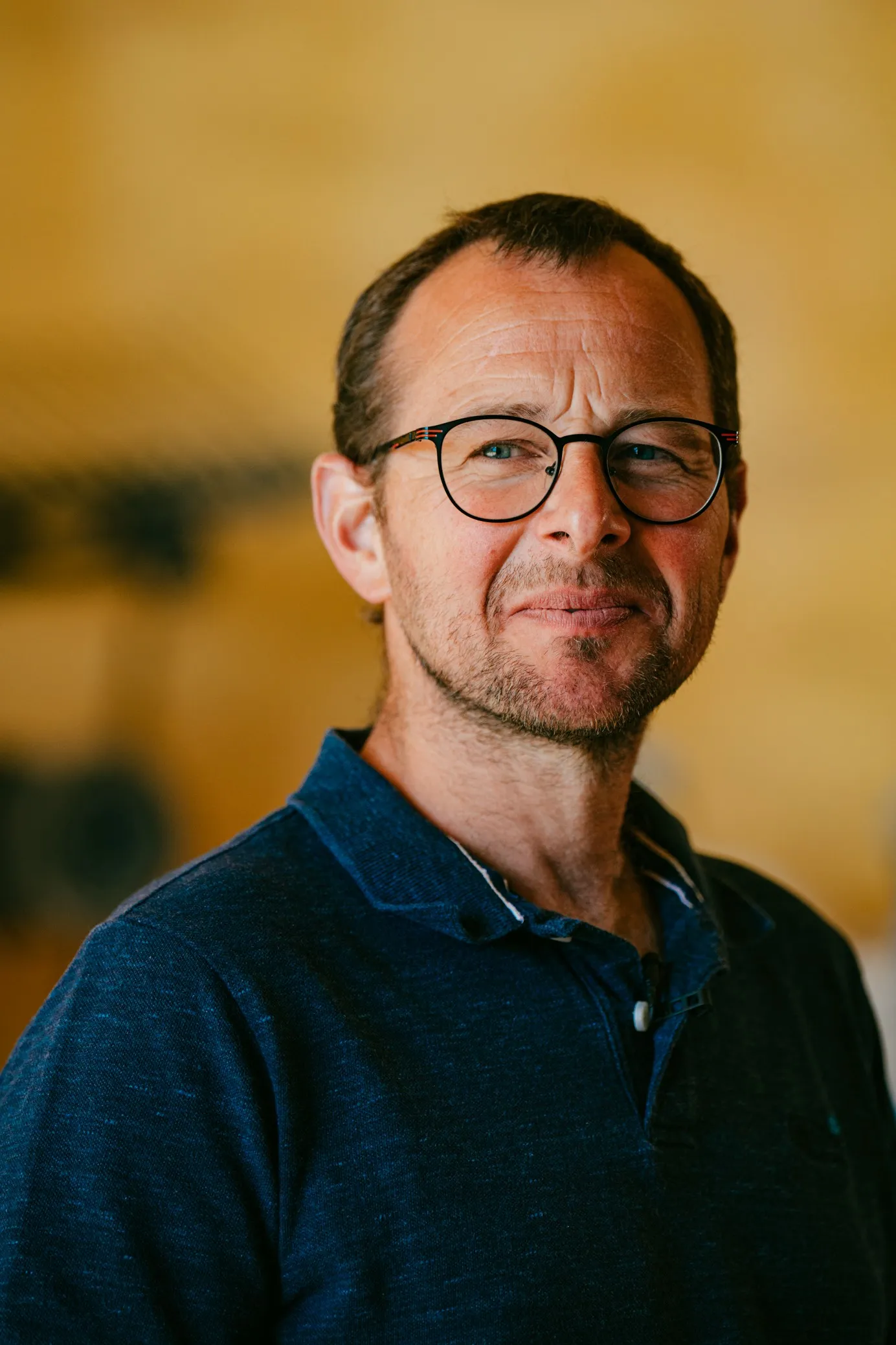 Portrait of a farmer with glasses in a navy polo, warm background, McCain regenerative agriculture