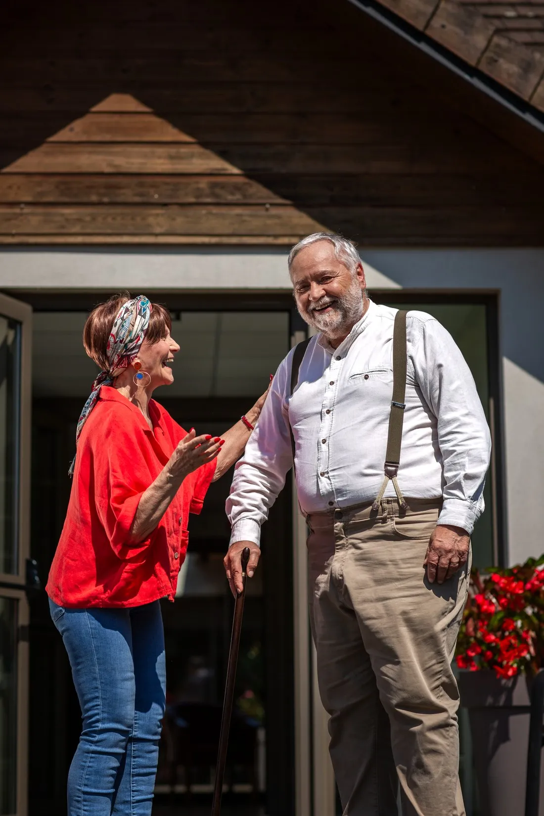 Woman in red and an older man with braces and a cane laughing outside a house, Mutualité sociale agricole