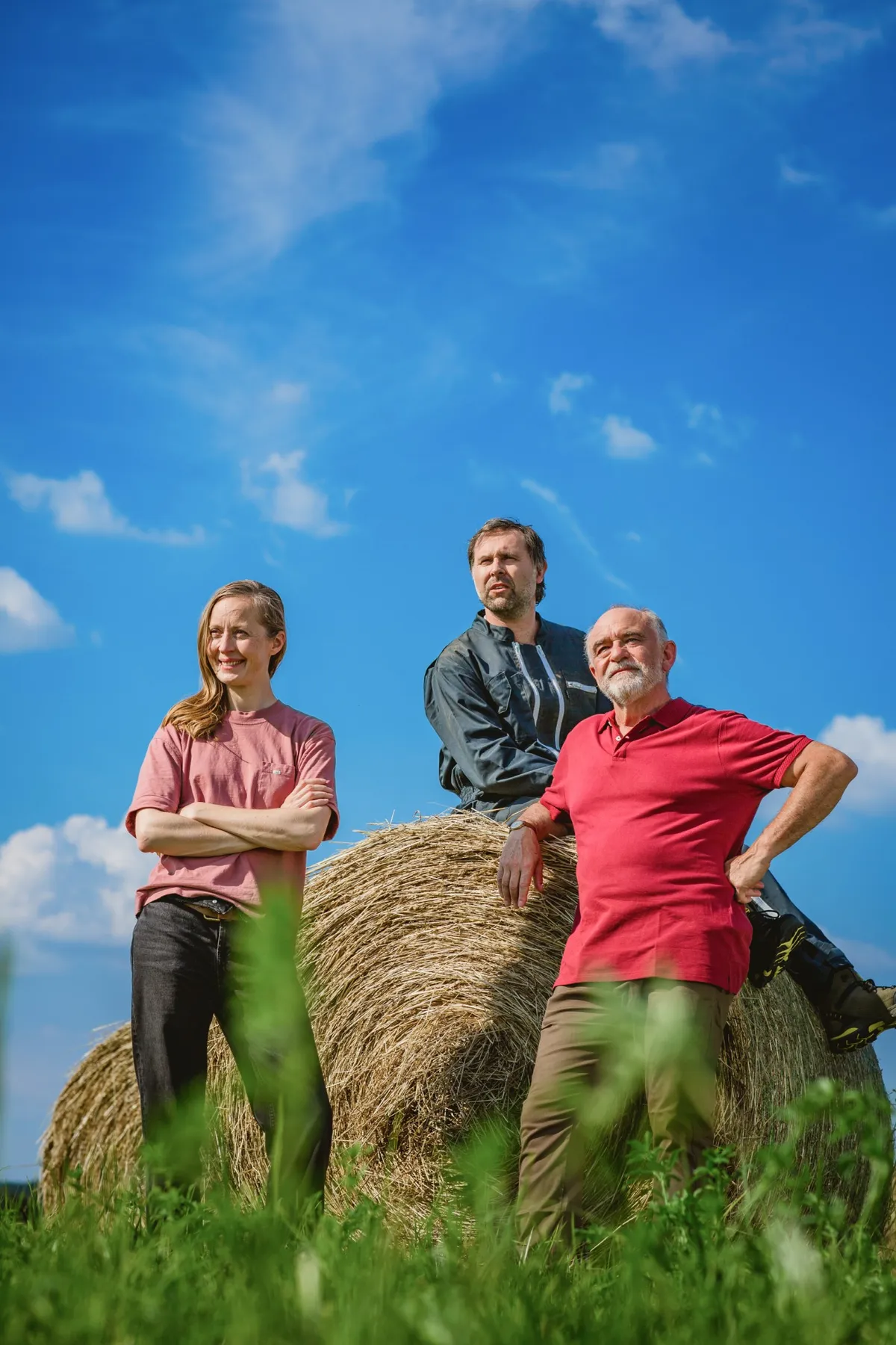 Three people posing by round hay bales under a bright blue sky, Mutualité sociale agricole campaign