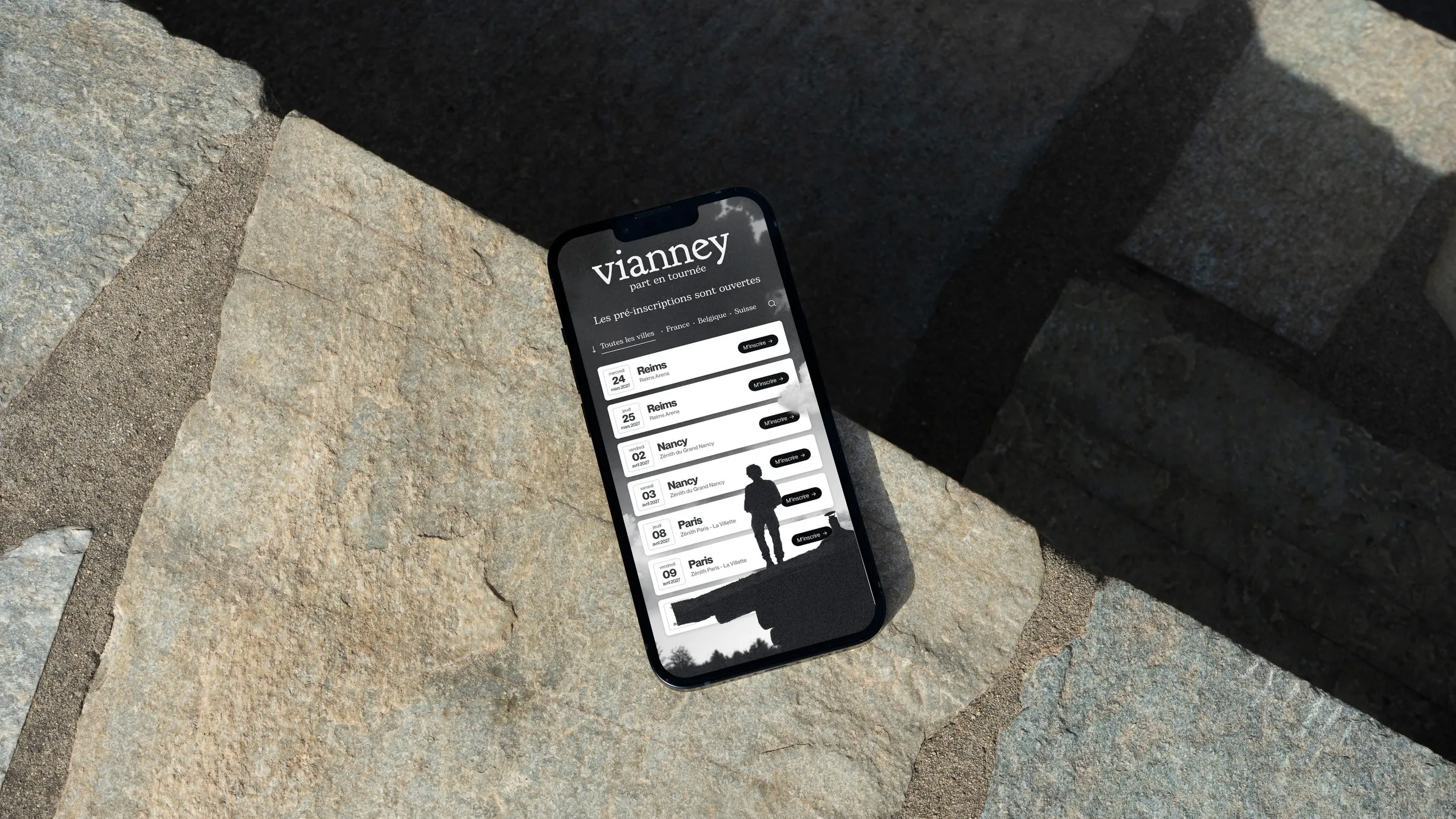 Phone lying on a stone slab, showing the mobile version of Vianney's tour website and its dates